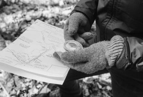 gloved hands holding a map and compass